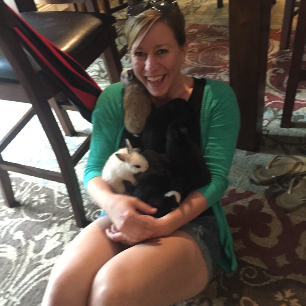 Ginny Dee sitting on the floor laughing with a lap full of bunnies—pure joy, silliness, and post-recovery chaos in its happiest form.