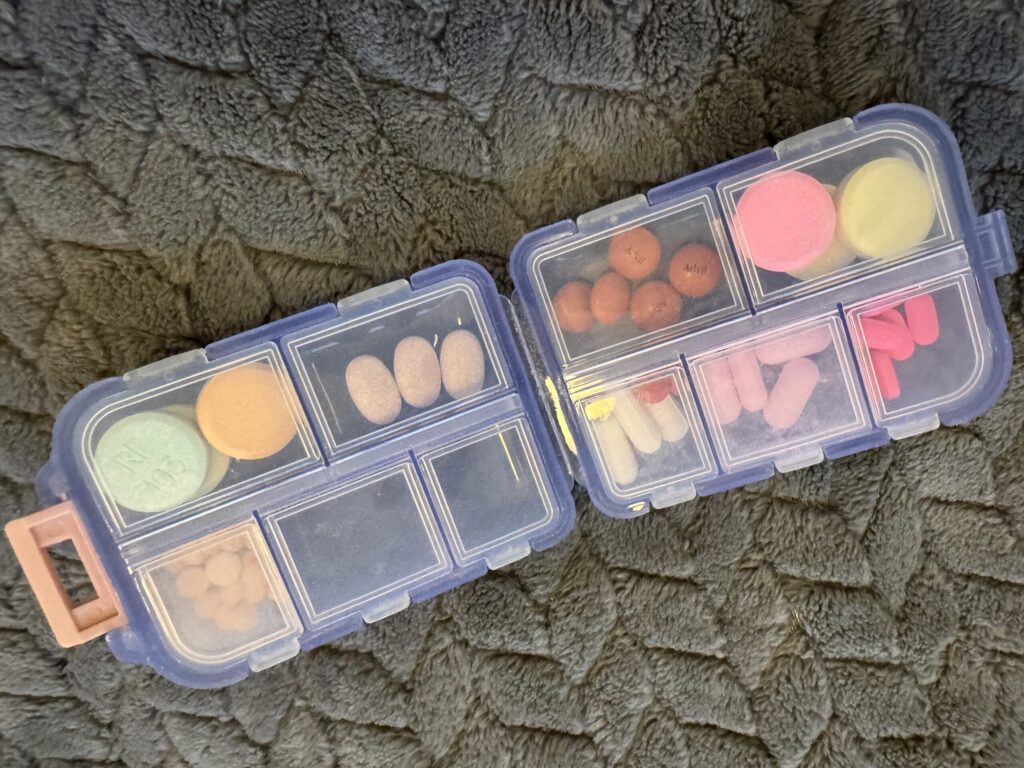 The 10-compartment pill box sits open on a grey blanket, colorful pills filling its slots.