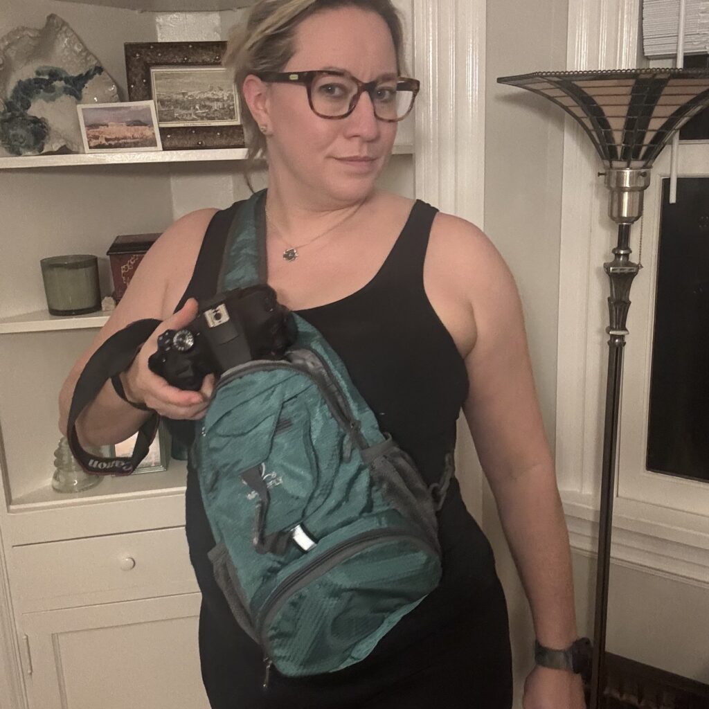 Ginny pulls her DSLR camera out of the sling bag she is wearing cross-body.