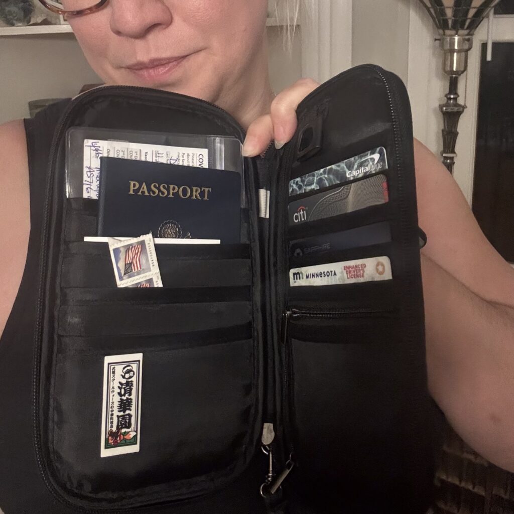 Ginny holds up her open travel wallet / organizer, which contains her passport, some stamps, credit cards, and a zippered pouch.