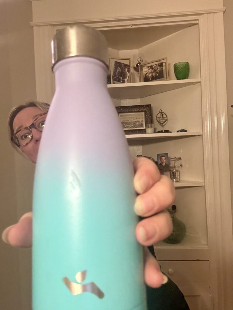 Ginny holds out her ombre purple-to-blue water bottle with silver details, peeking our from behind it.