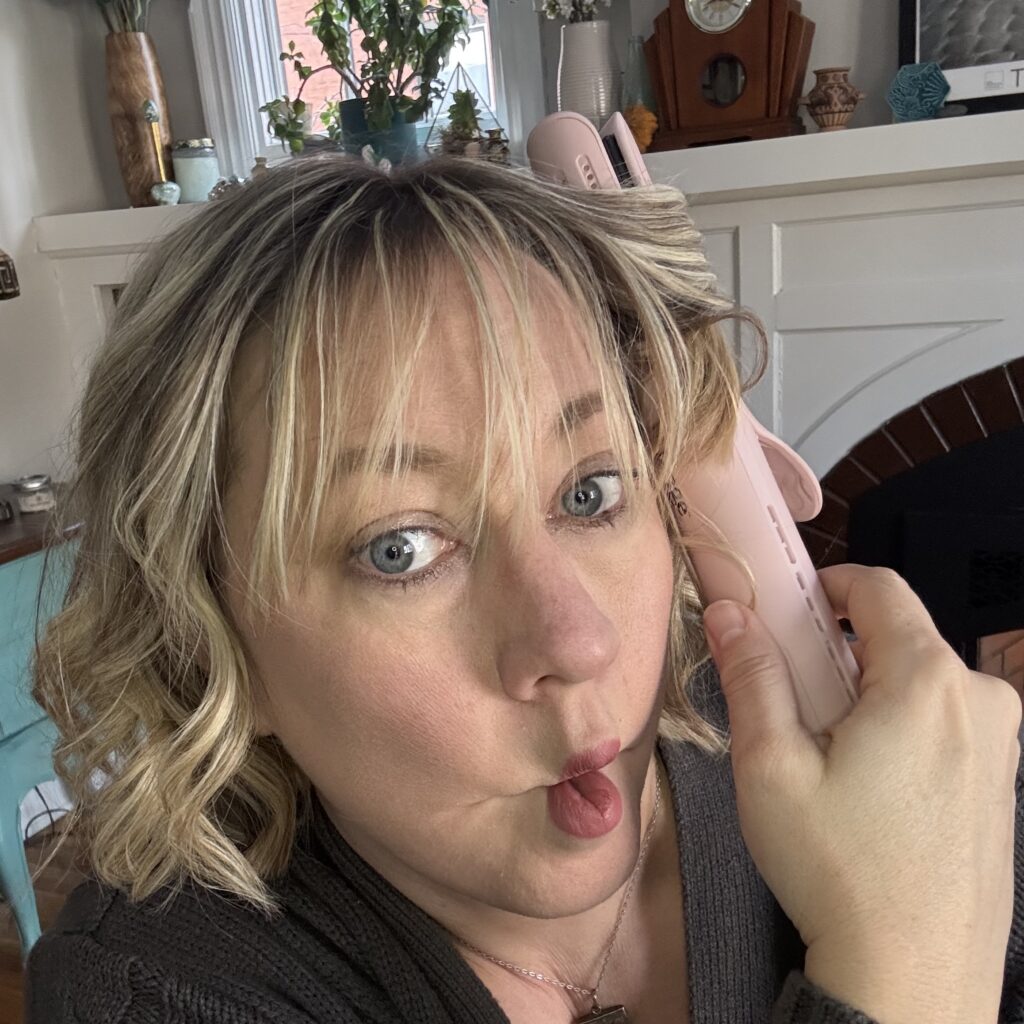 Ginny makes a funny fish face as she uses the small pink curling iron in her living room for some reason.