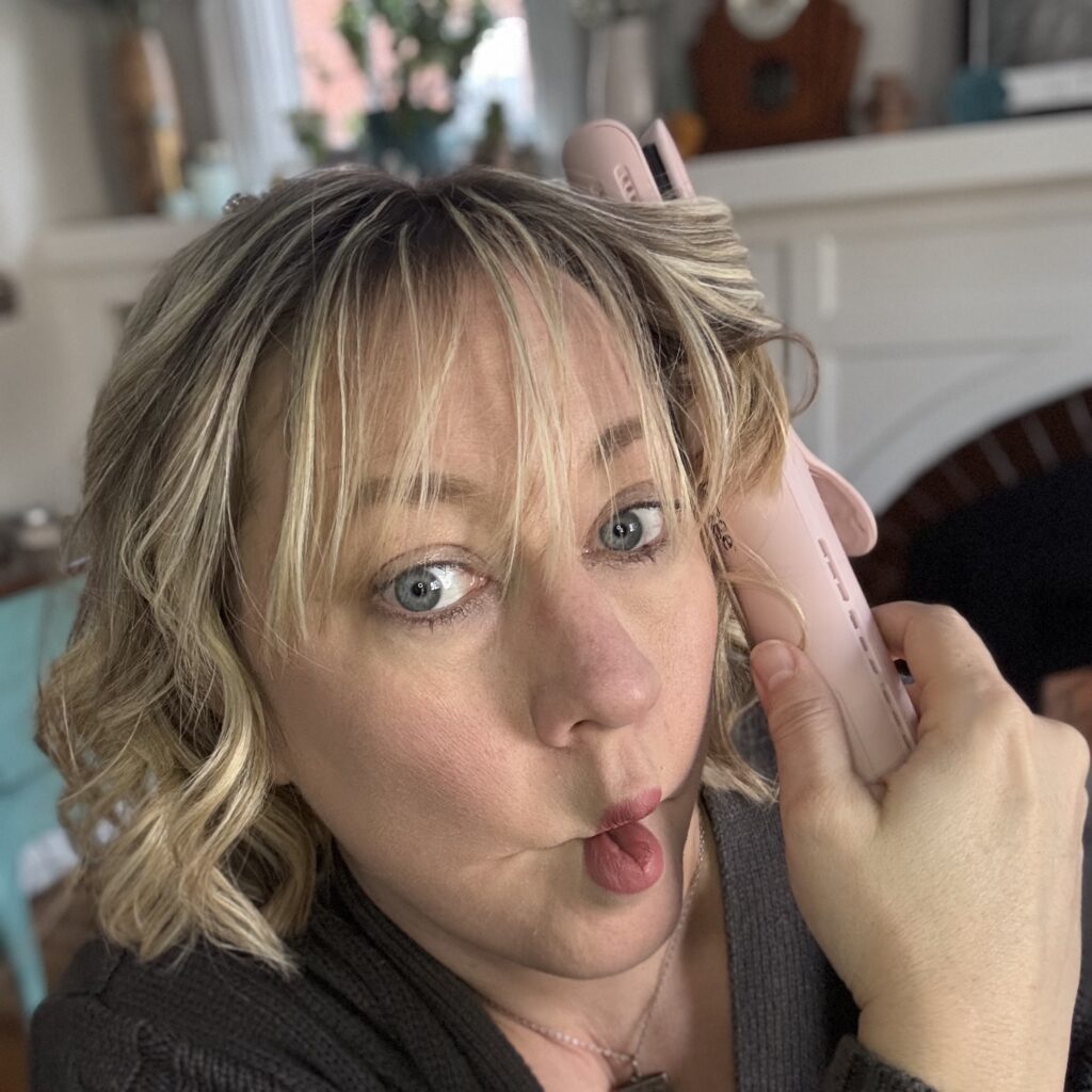L’ANGE Le Duo 360° Airflow Styler flat/curling iron — dual-purpose travel hair tool with built-in cooling vents for lasting curls. Being used by Ginny, who is making a fishy face.