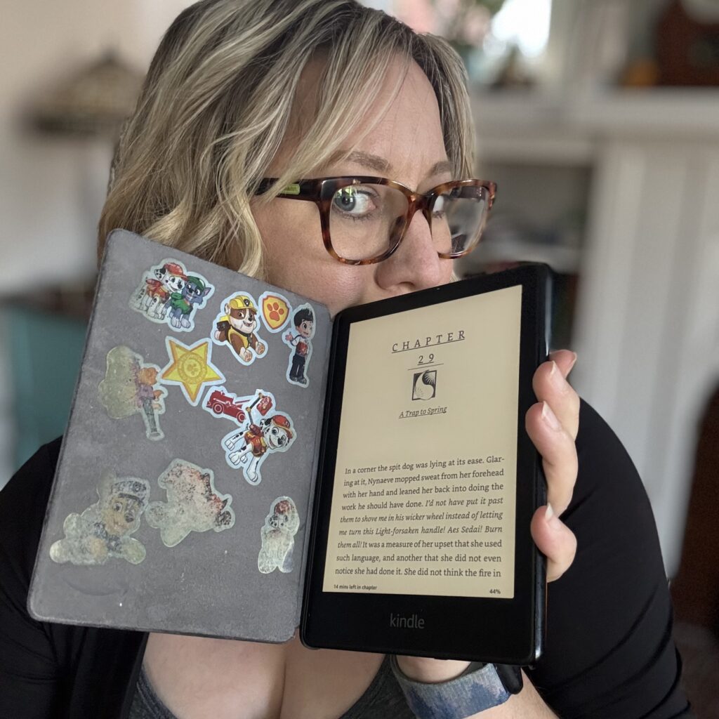 Ginny holds up her kindle, turned on to show the first page of a chapter, in its case so you can see the Paw Patrol stickers her niece and nephew have added.
