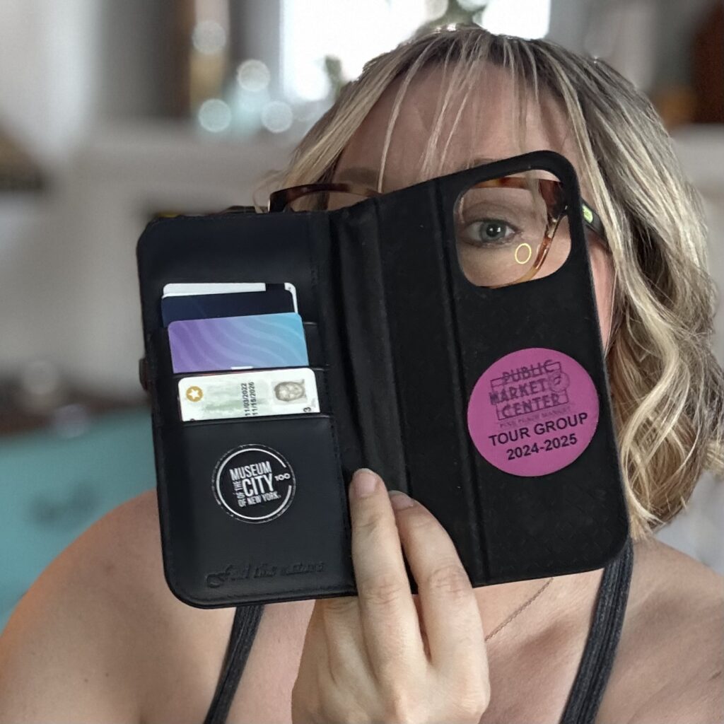 Ginny peers through the camera hole in the outer case with one eye, as it holds various cards and displays stickers from old tours.