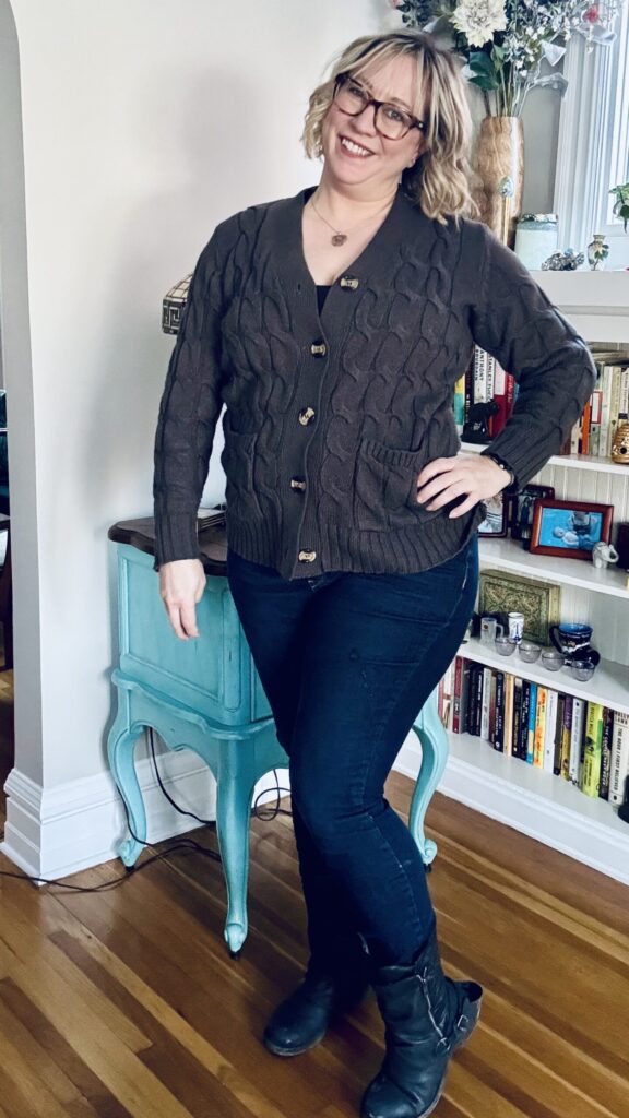 Ginny wearing the cool-weather travel outfit:  dark gray cable-knit button up sweater, skinny jeans, and black mid-calf boots over them.