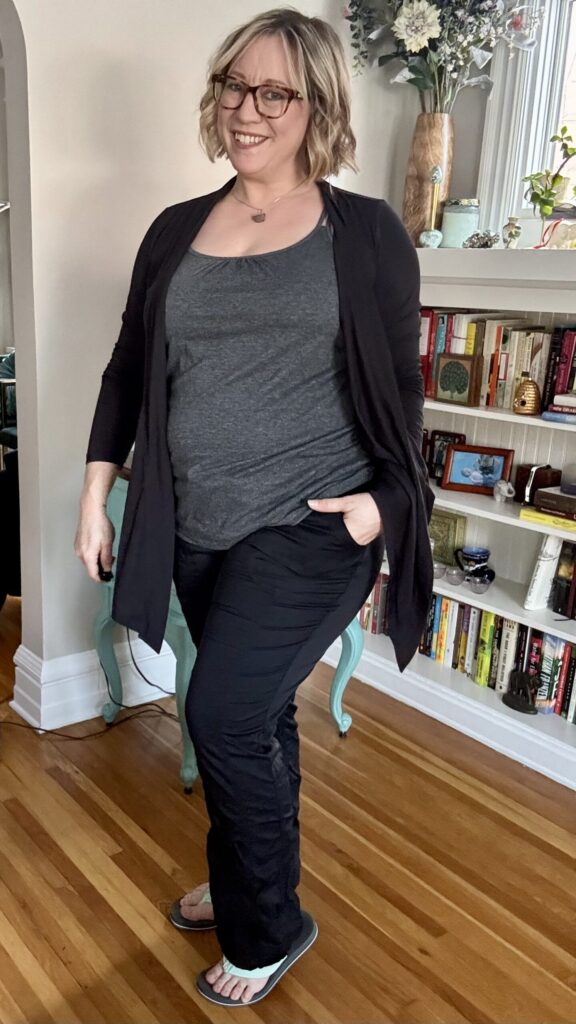 Ginny wearing the warm-weather travel outfit:  a dark gray tank top, thin black wrap sweater, black nylon pants, and flip flops.