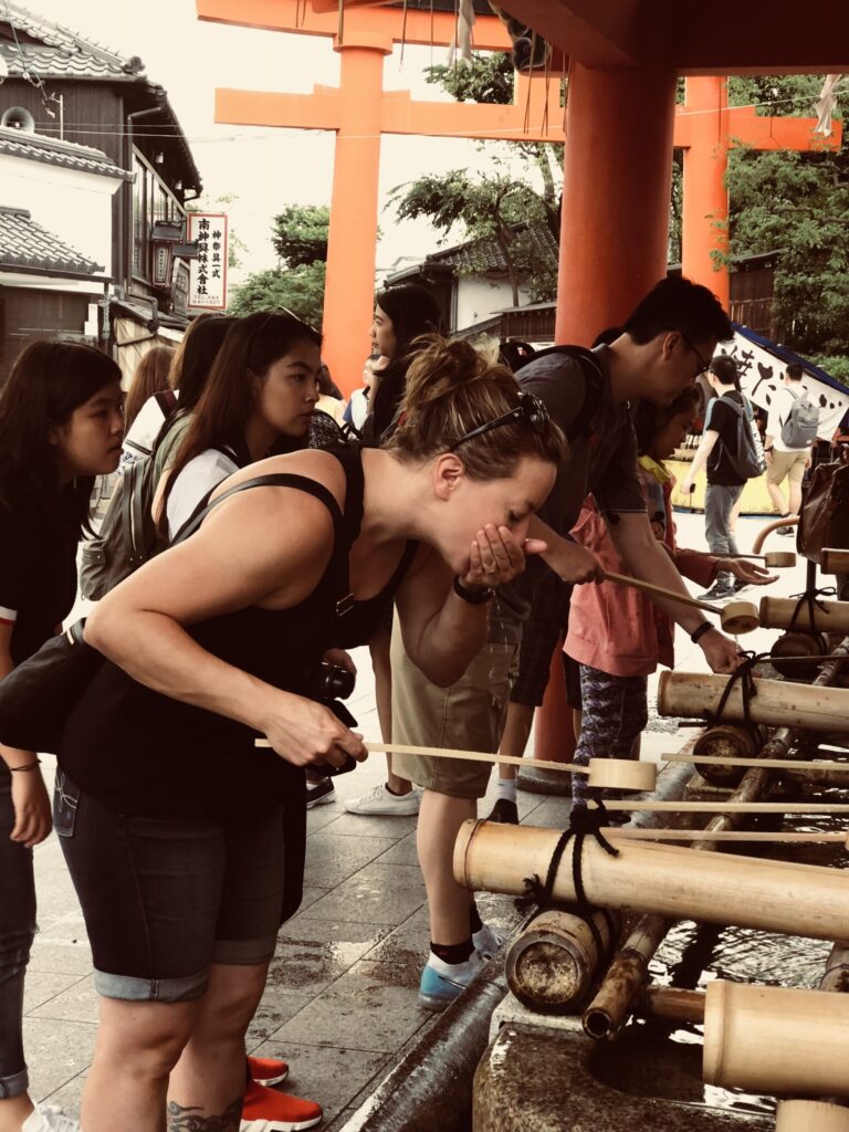 Ginny rinsing her mouth at a Japanese temple—participating in the traditional purification ritual with respect and curiosity