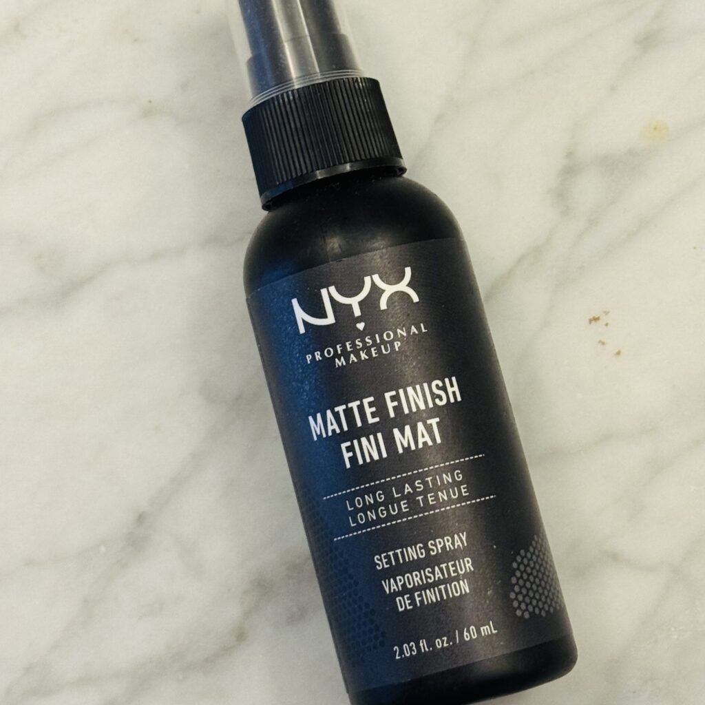 The small, black bottle of NYX Matte Finish Setting Spray that makes Ginny's makeup last all day.