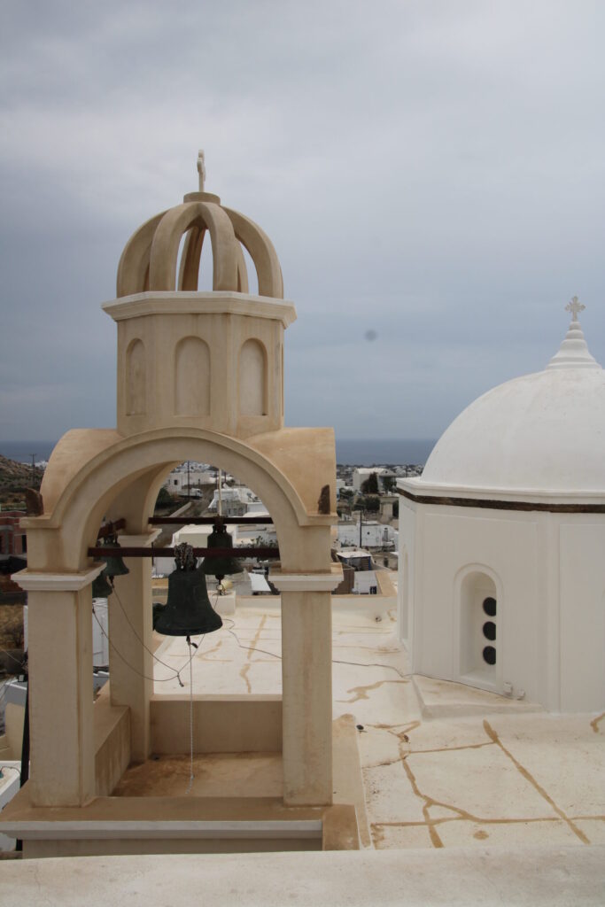 View from the roof of Agios Spyridonos Church in Emporeio, showing its pale dome and bell tower in the foreground, with sweeping views of the surrounding Venetian castle ruins and the sea in the background
