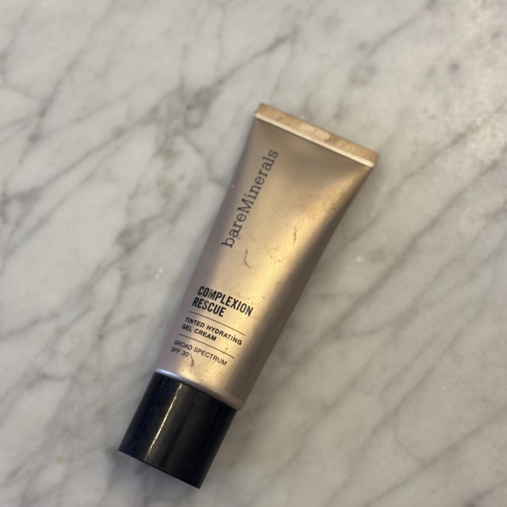 bareMinerals Complexion Rescue tinted moisturizer sits on a grey marble countertop, waiting to give Ginny's skin a glow up.