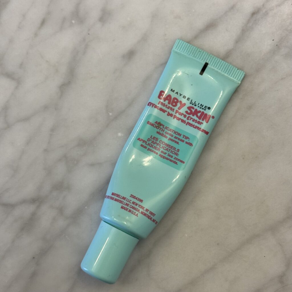 A little turquoise tube of magical Maybelline Baby Skin primer sits on a gray marble counter - ready to sweep a filter over Ginny's skin.