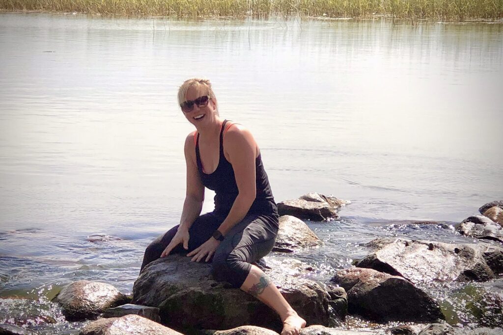 Ginny laughing beside the Mississippi headwaters after slipping on the rocks—joyful moment from a sober travel adventure