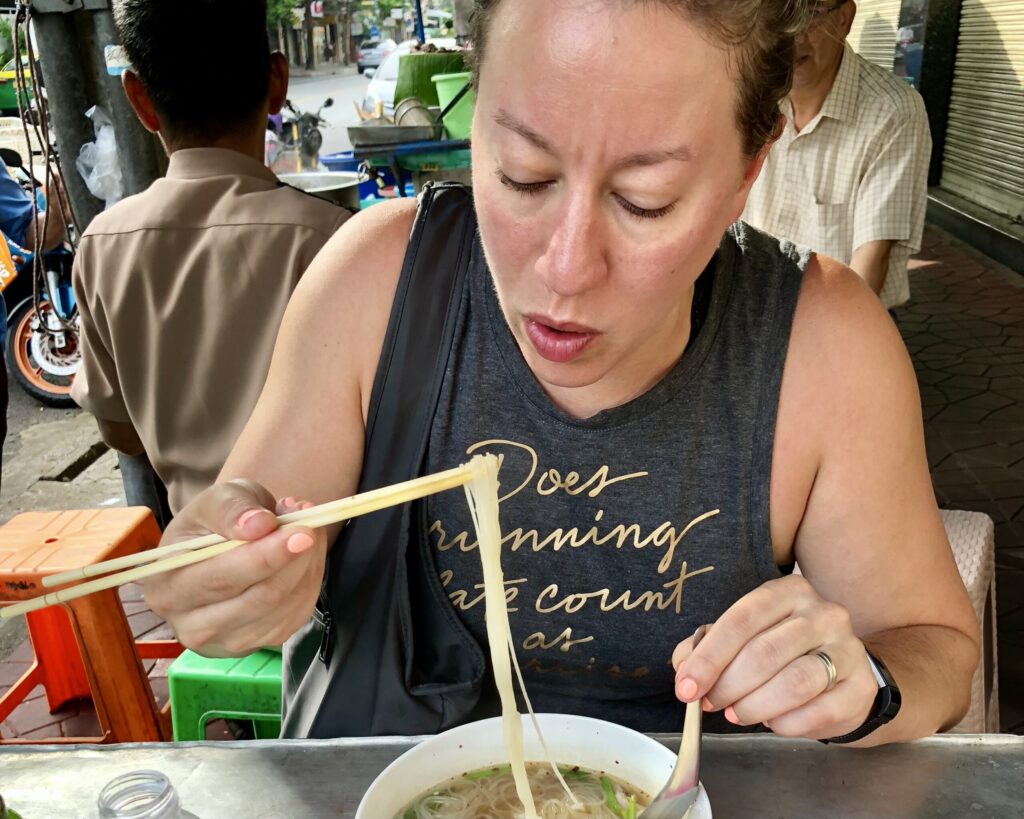Ginny eating pho at a street stall in Thailand—an authentic cultural experience that is rich in flavor, light on cost