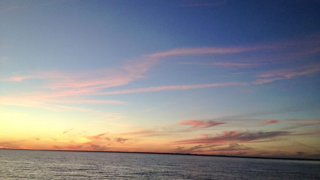 Sunset over calm ocean waters, with soft pink and gold clouds streaked across a peaceful evening sky — a tranquil, open horizon symbolizing hope and healing.