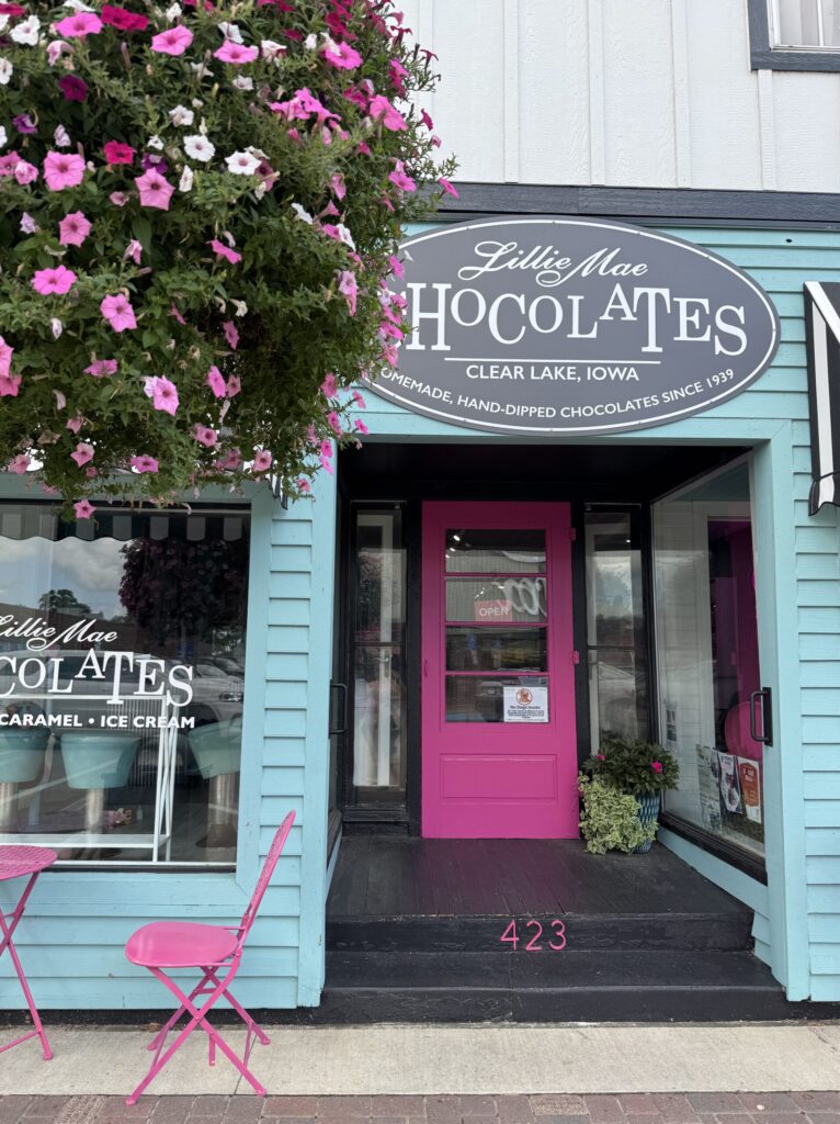Lillie Mae Chocolates storefront on Main Street, Clear Lake, Iowa—teal siding and pink door with café seating.