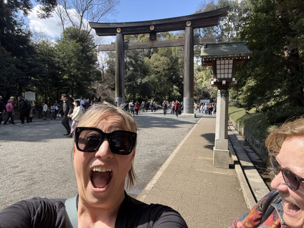 Ginny Dee smiling with joyful abandon in front of a towering torii gate in Japan—a portrait of sober travel, curiosity, and unexpected delight.