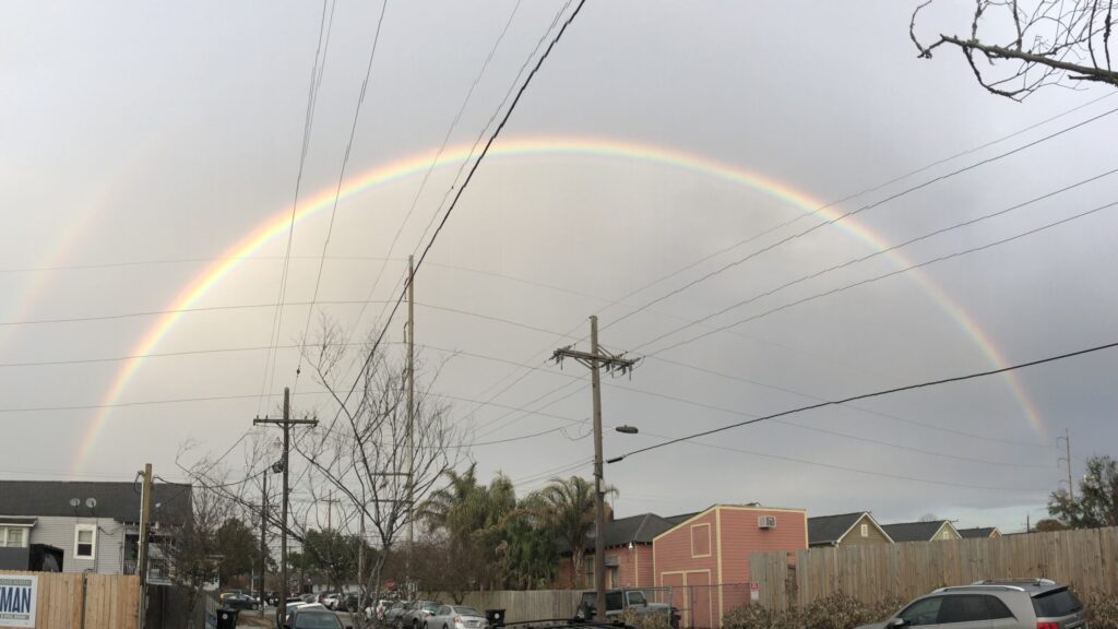 A rainbow arcs over a cluttered New Orleans street, symbolizing unexpected beauty and hope in the middle of real-life chaos.