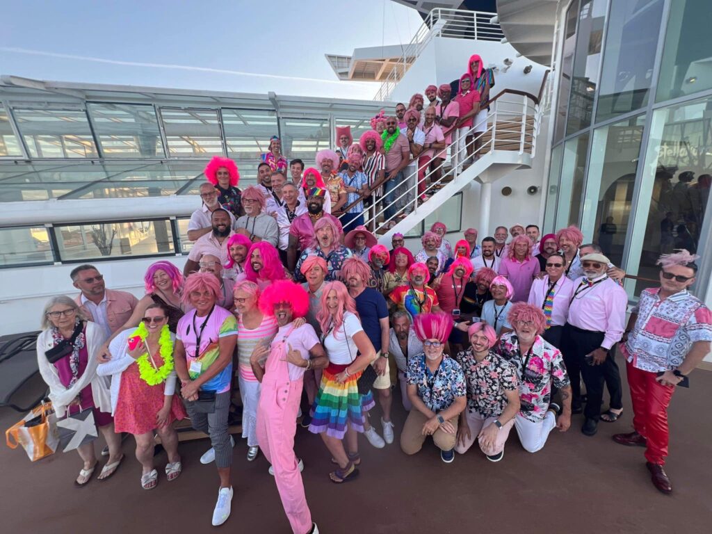 Fellow-Ship cruise group dressed in pink wigs and costumes, laughing and posing on deck.