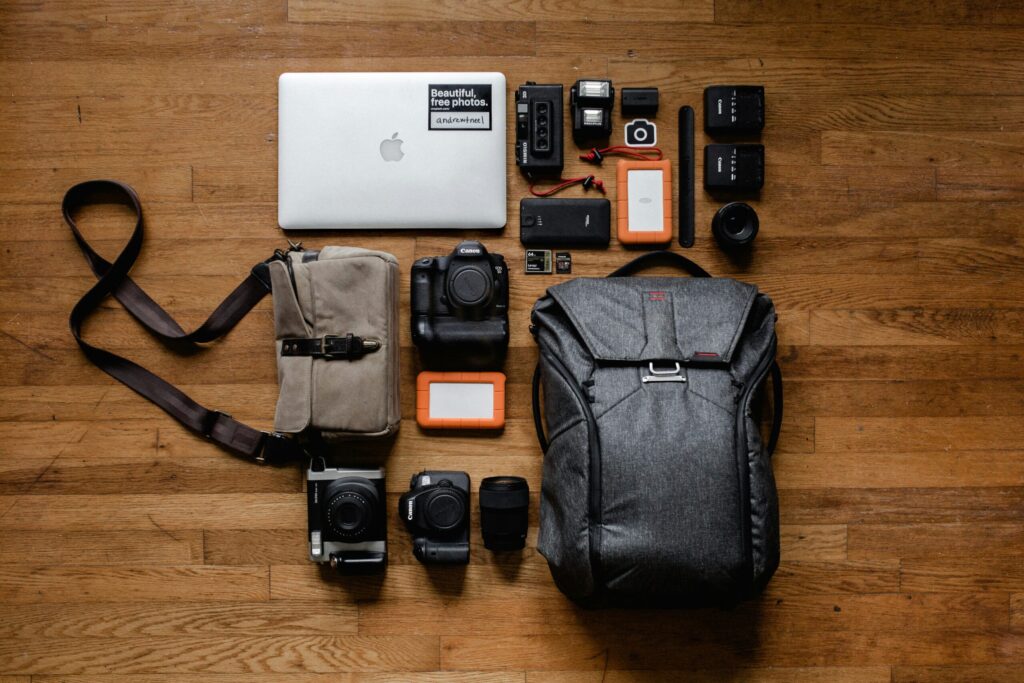 Organized flat lay of travel electronics and camera gear, including laptop, chargers, and backpack, arranged for packing.