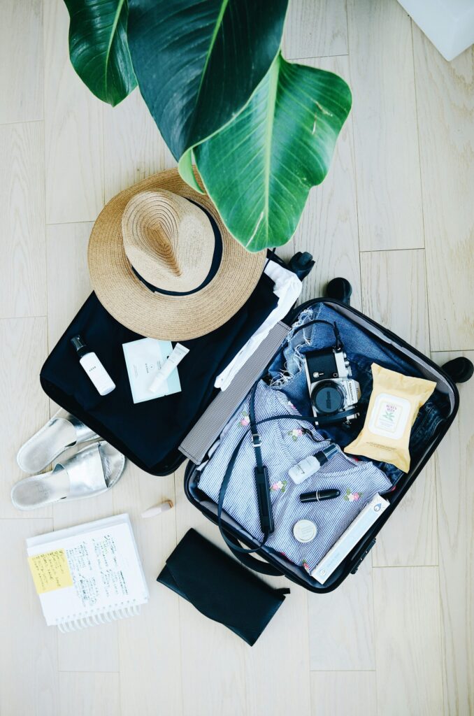 Stylish flat lay of a suitcase with clothes, a straw hat, camera, and toiletries, ready for packing on a long trip.