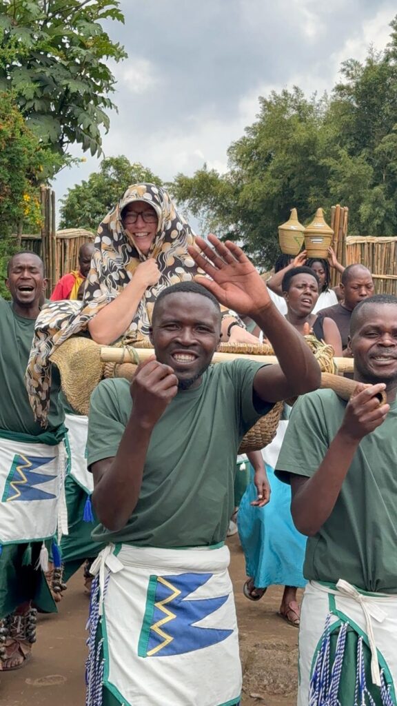 Ginny is carried in a litter by four men while demonstrating a traditional marriage ceremony in a cultural village in Rwanda.