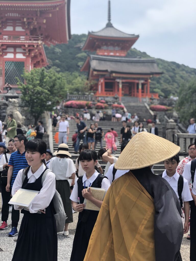 People in conservative and traditional clothing, including a farmer-style straw hat, in front of Kiyomizu-dera temple in Kyoto.