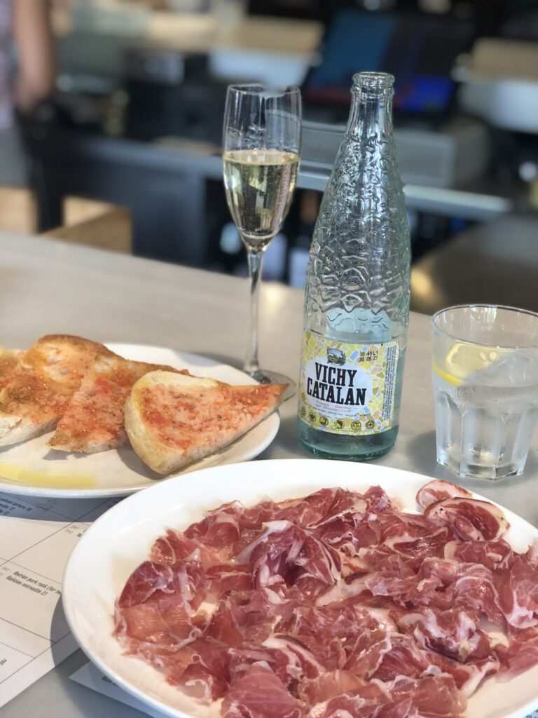 A tabletop bearing jamon iberico, pan con tomaté, and Vichy Catalan.