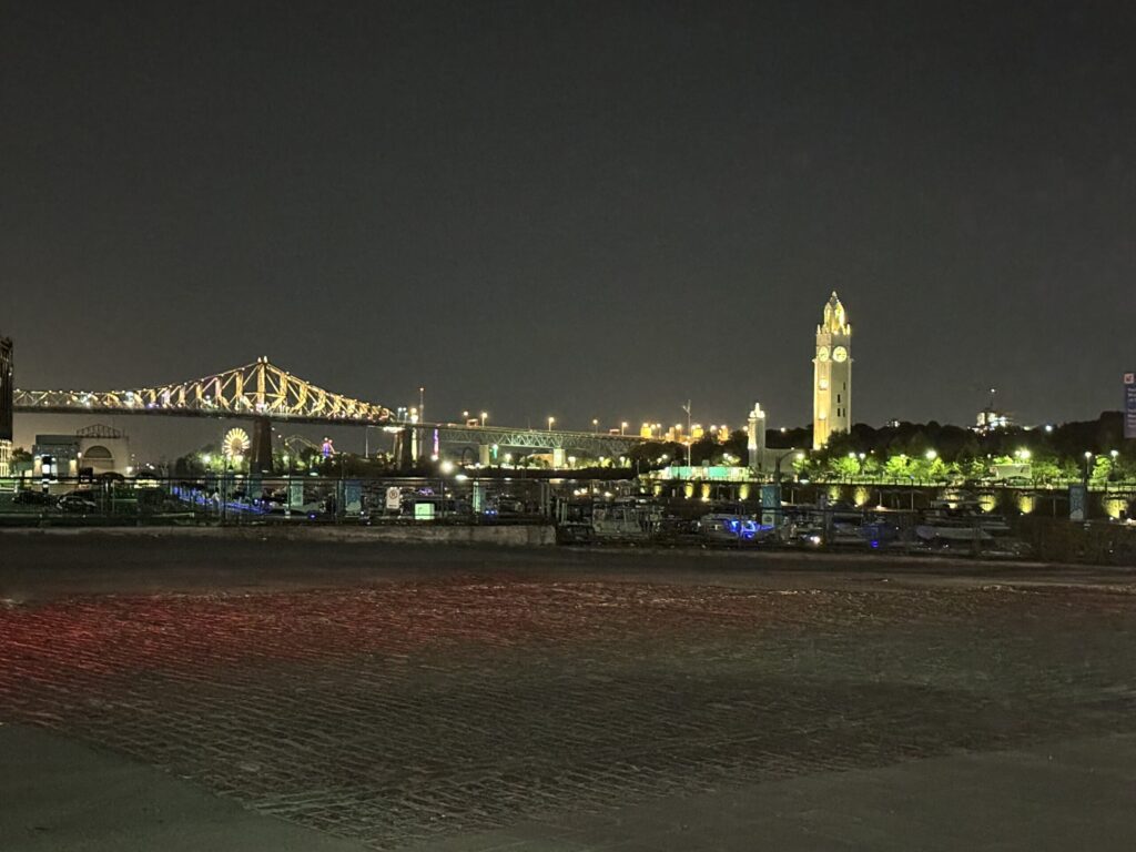 Nighttime view of the Old Port of Montreal, including twinkling lights on a clocktower and a bridge.