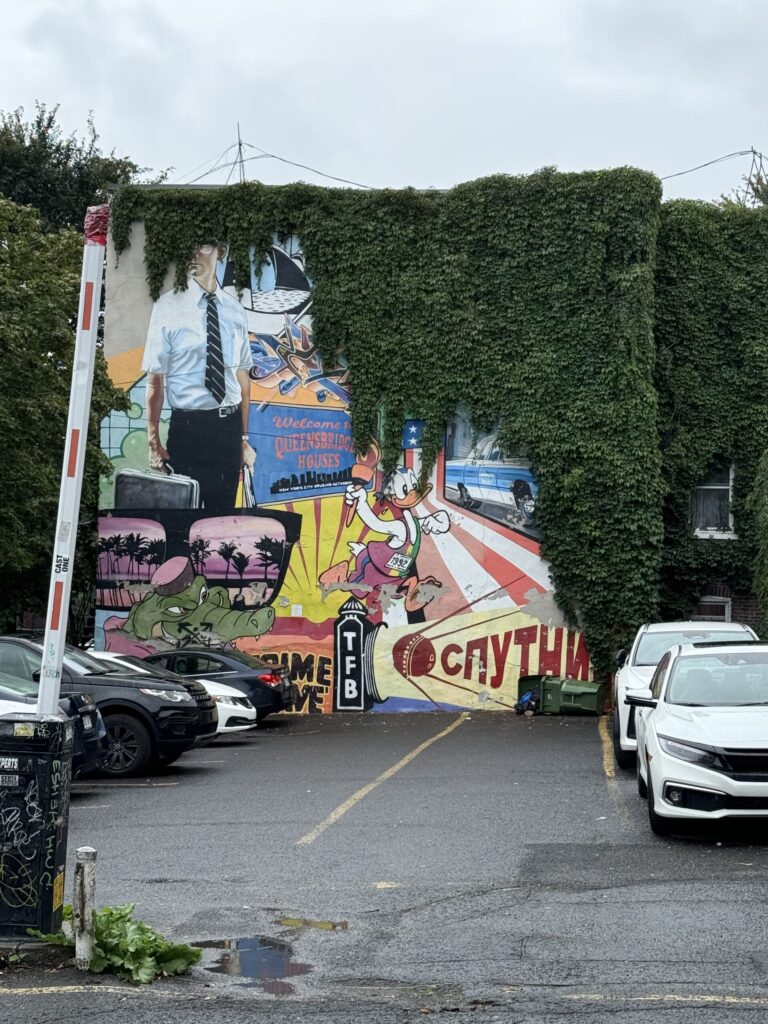 A beautiful street art wall mural half covered in vines in Montreal.