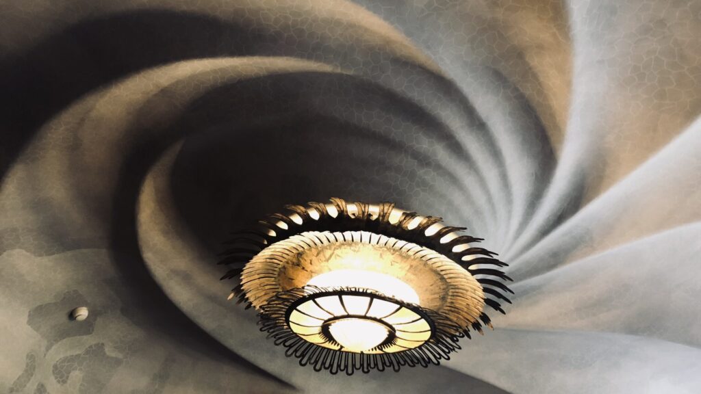 A unique chandler on a ceiling with a raised shell-like swirl from one of Saudi's famous houses in Barcelona, Casa Batillo.