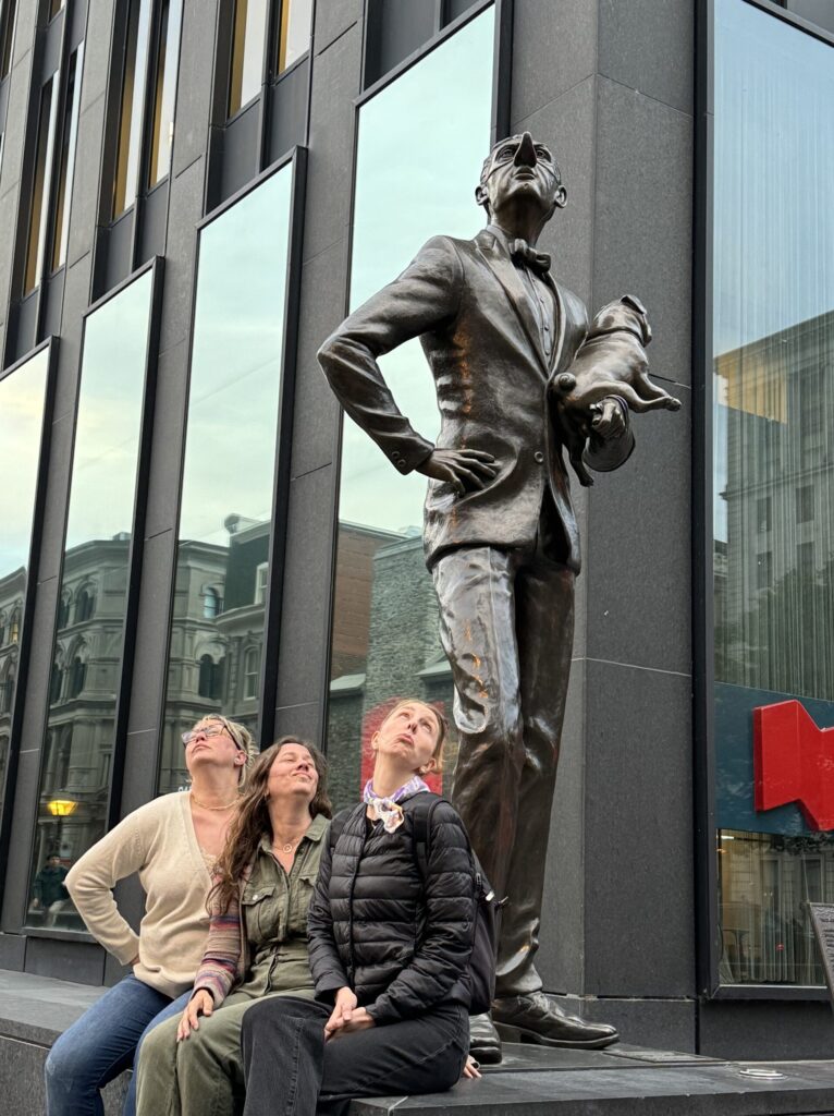 Ginny and two of her gals pose with noses in the air in front of a statue of a man with his overly large nose in the air in Montreal.