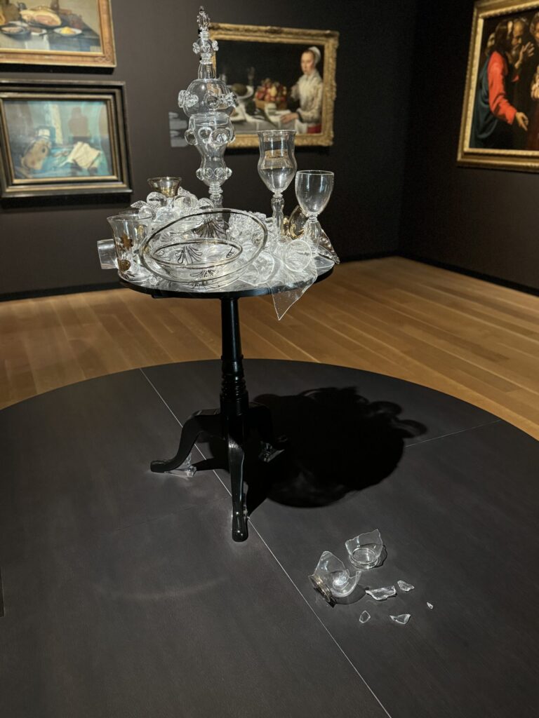 An art installation of a black table covered in glassware, some of which is broken or spilled on the floor, but which was not broken by Ginny herself, at Montreal Museum of Fine Arts.