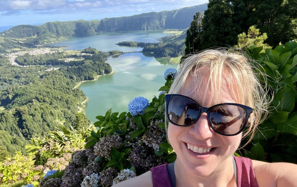 Ginny smiles for the camera in front of blooming hydrangeas and Lagoa Azul and Lagoa Verde, two brightly hued lakes in the caldera of a volcano on Sao Miguel Island in the Azores.