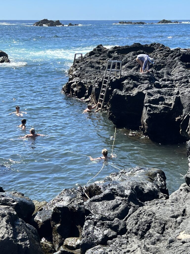 Ginny holds on to two ropes in Termas da Ferraria on the western tip of São Miguel Island in the Azores, as cold waves rush in and hot spring water rushes out.