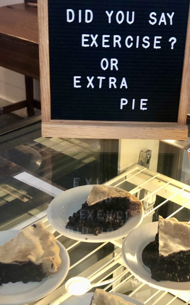 Blueberry pie slices in Maine, under a sign that reads "did you say exercise or extra pie".