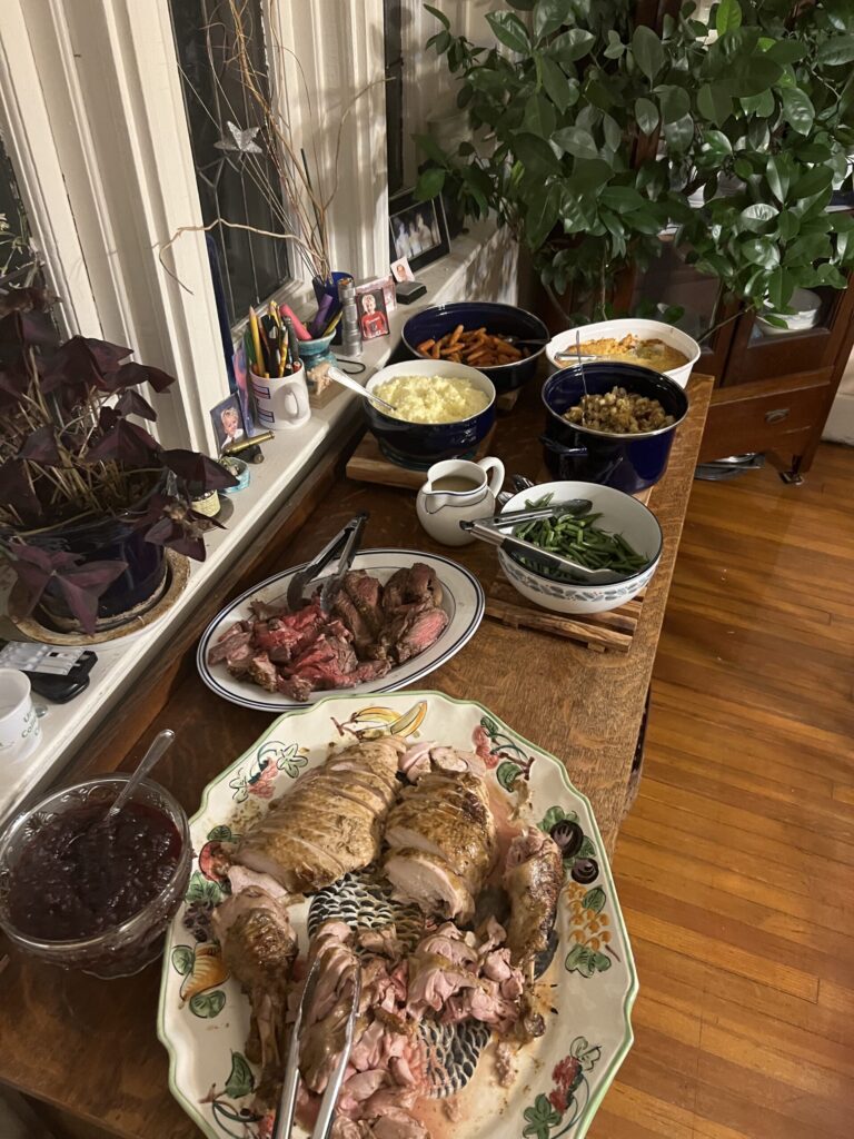 Holiday dinner spread with turkey, roast beef, vegetables, mashed potatoes, and sides on a wooden table.