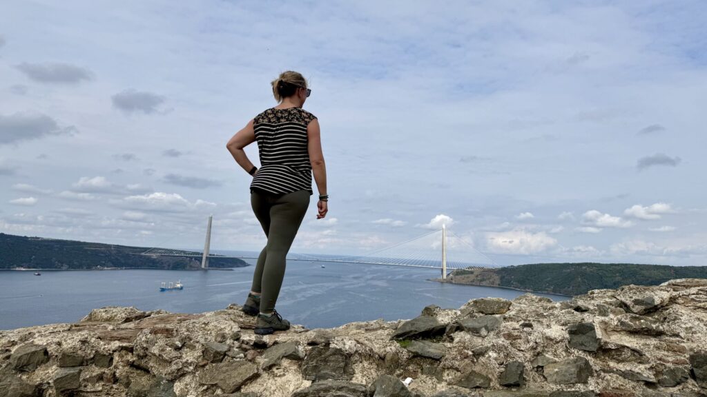 Ginny stands on the crumbling rock wall of a castle with her back to the camera, looking out to the Black Sea from high above - the destination of her journey down the Bosphorus that took her on many random side quests.