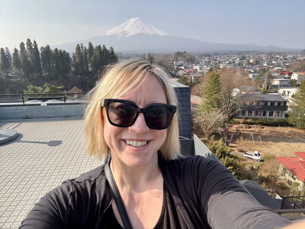 Ginny smiling with Mount Fuji rising above the town of Fujikawaguchiko, Japan, on a clear spring day.