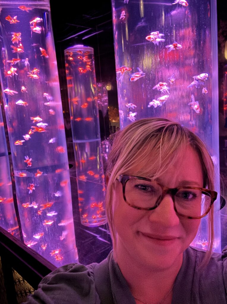 Ginny exploring the Art Aquarium in Tokyo, surrounded by illuminated goldfish displays and colorful light installations.