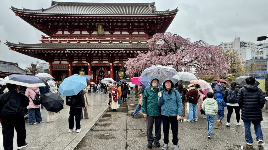 Ginny's parents standing in the rain in front of Senso-ji Temple during cherry blossom season in Tokyo, Japan.